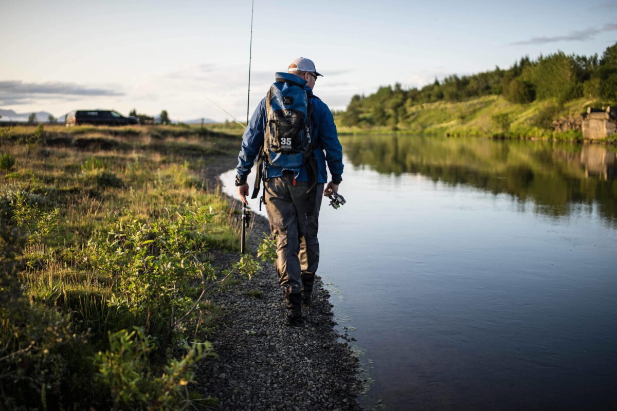 Maður gengur með veiðistangir eftir árbakka